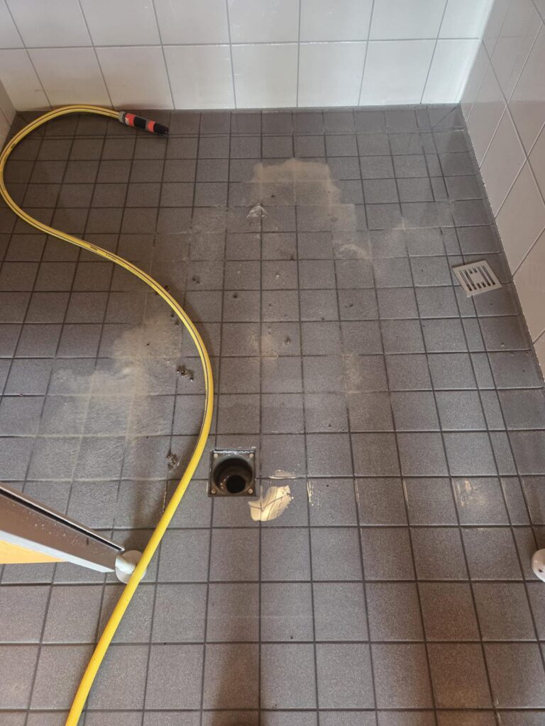 Nasser Fliesenboden mit Wasserschlauch im Sanitärbereich