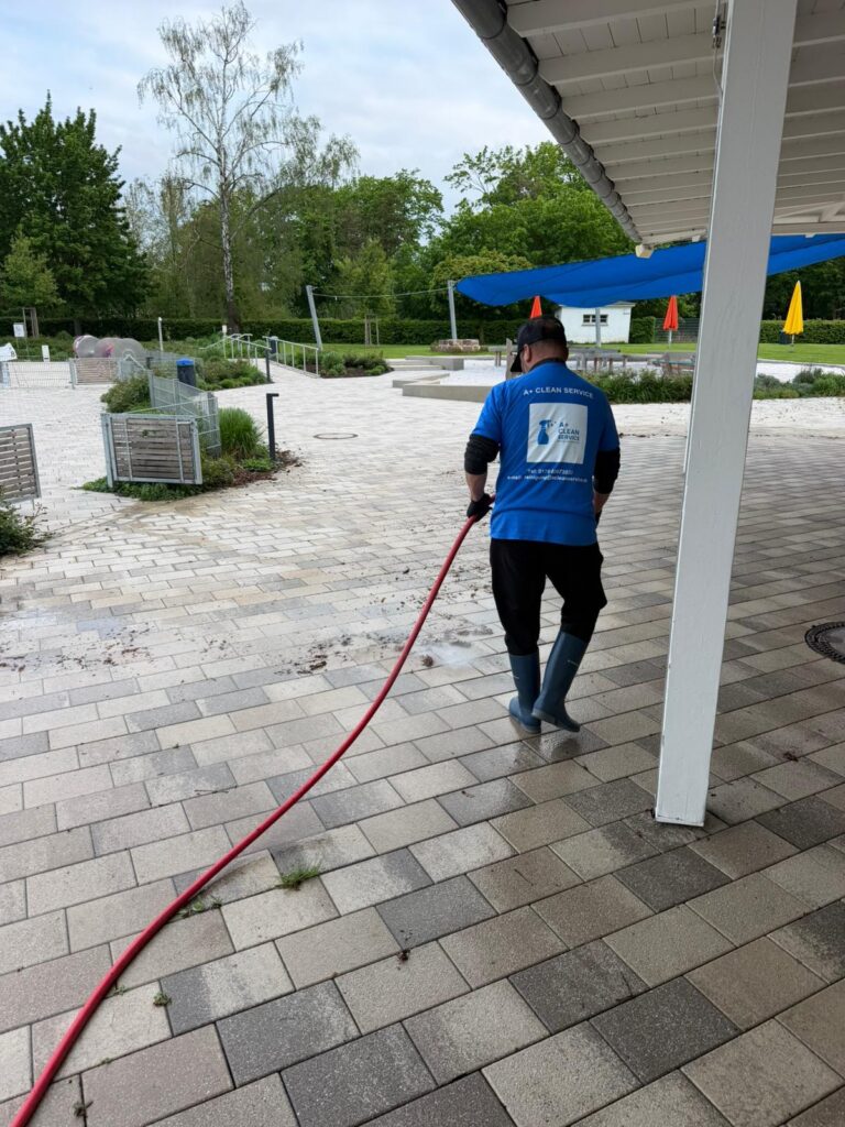 Mitarbeiter bei der Pflege der Außenanlagen mit dem Wasserschlauch